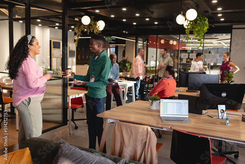 Multiracial businessman and businesswoman discussing while having coffee during break in office