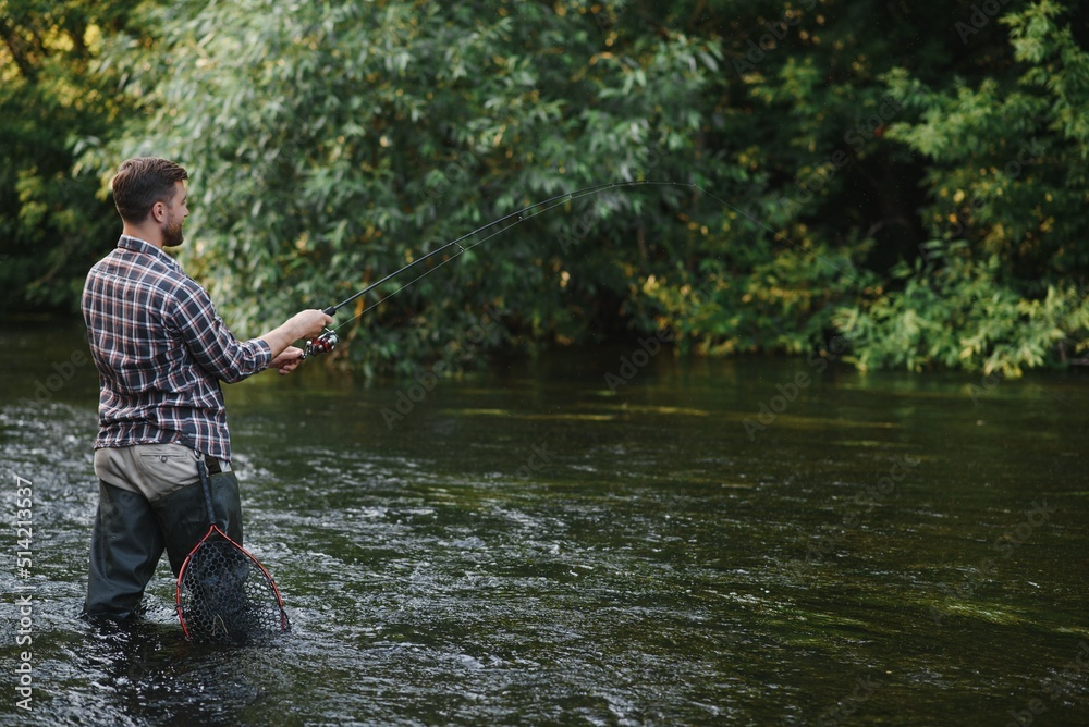 Fisherman catches a trout on the river in summer Fisherman catches a trout on the river in summer
