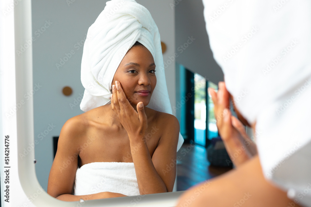 African american young woman touching her cheek while looking in mirror at home African american young woman touching her cheek while looking in mirror at home