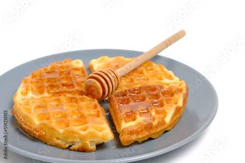 Soft muffin waffles poured with fresh honey using honey spoon, in plate on white background. © freeman83