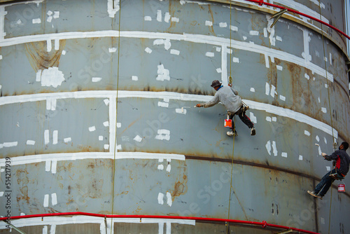 Industrial rope access worker hanging from tank oil shell plate