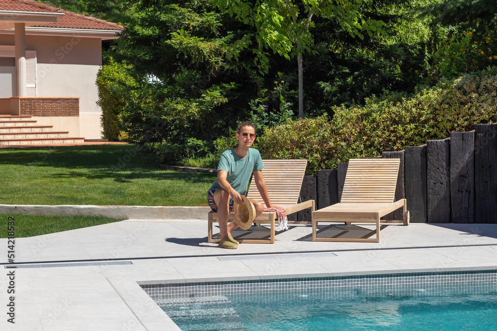 Young man sitting relaxed on a sun lounger in his garden pool on a hot summer day
