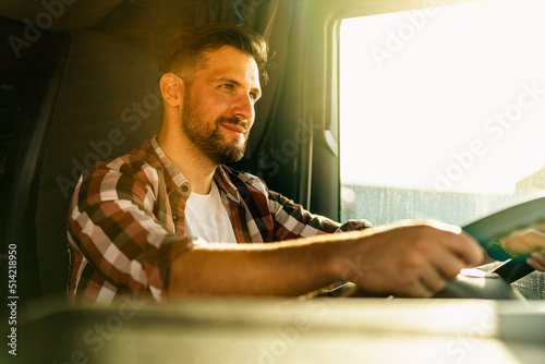 Professional middle aged truck driver in casual clothes driving truck vehicle going for a long transportation route. photo