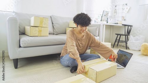 An Asian happy woman girl working online from home, selling product, packing postal parcel packaging carton box delivery, in social media. Online shopping business. SME ecommerce. People lifestyle.
