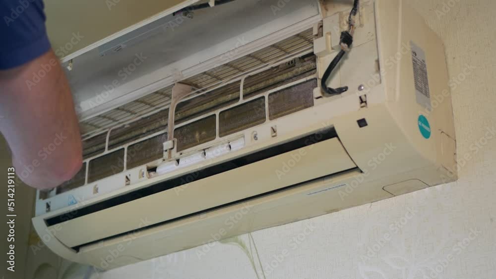 A man cleans the air conditioner from dust with a brush, cleaning the split system. A man cleans the air conditioner from dust with a brush, cleaning the split system.