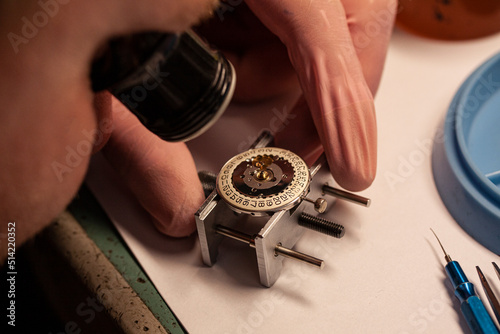 Watch repair at watchmaker wiyh magnifying glass. Focus on date disc inside case. Maintenance of clockwork. Selective focus close-up image. photo