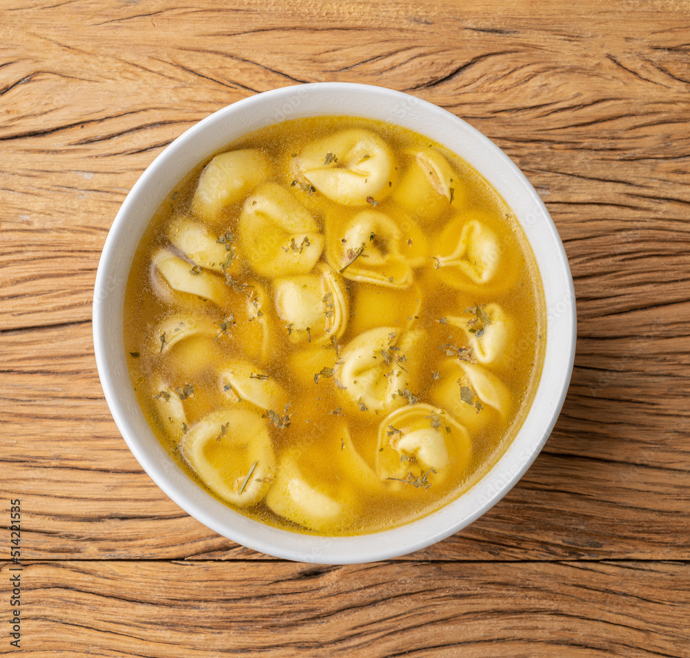 Cappelletti or tortellini brodo soup in a bowl over wooden table Cappelletti or tortellini brodo soup in a bowl over wooden table