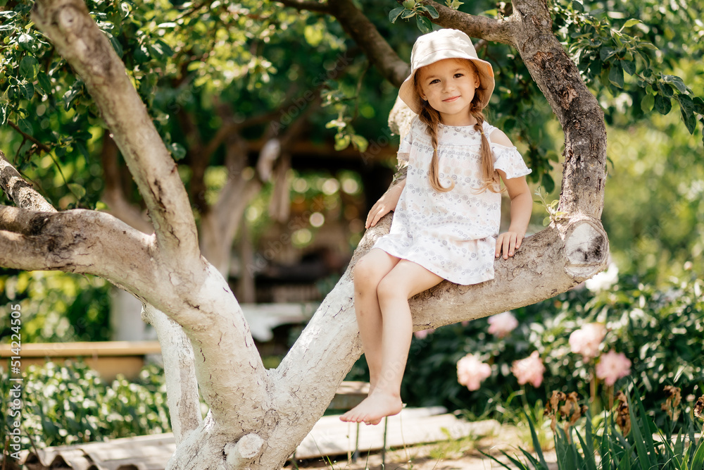 Small girl climb tree in summer garden, activity. Little girl on tree branch, childhood. Vacation, activity, lifestyle. Kid fashion, style, beauty Childhood youth growth