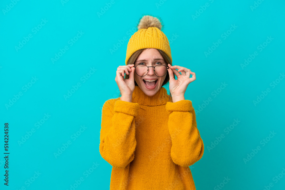 Young English woman wearing winter jacket isolated on blue background with glasses and surprised Young English woman wearing winter jacket isolated on blue background with glasses and surprised