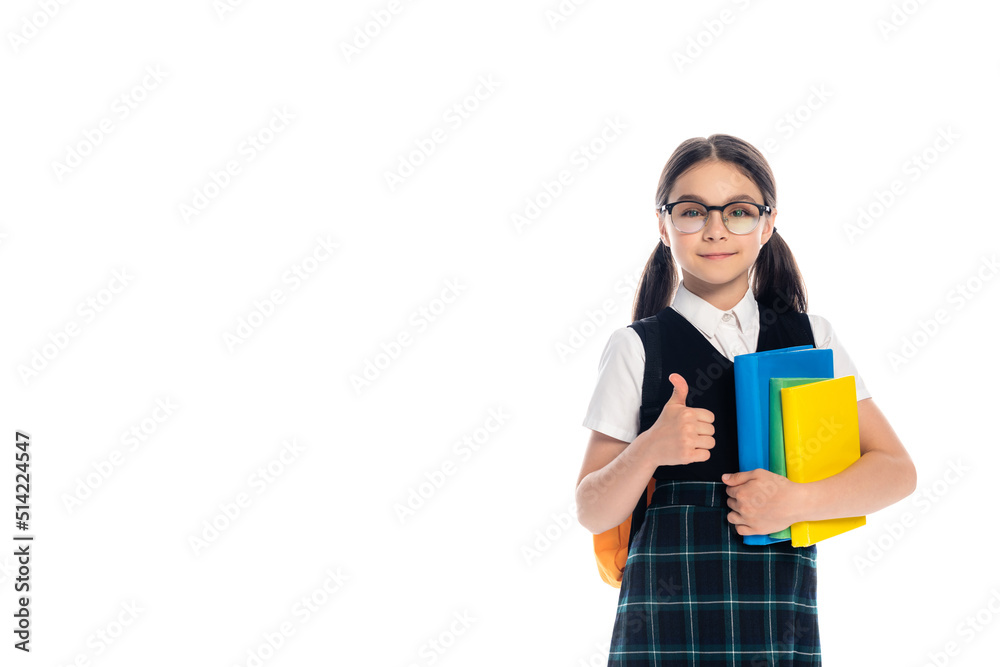 Pupil in eyeglasses holding books and showing thumb up isolated on white.