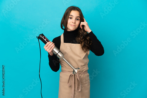 Little girl using hand blender isolated on blue background thinking an idea