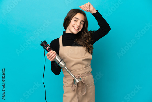 Little girl using hand blender isolated on blue background celebrating a victory
