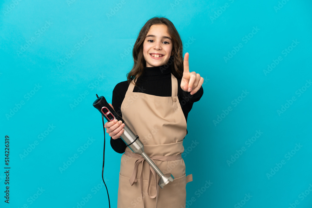 Little girl using hand blender isolated on blue background showing and lifting a finger Little girl using hand blender isolated on blue background showing and lifting a finger
