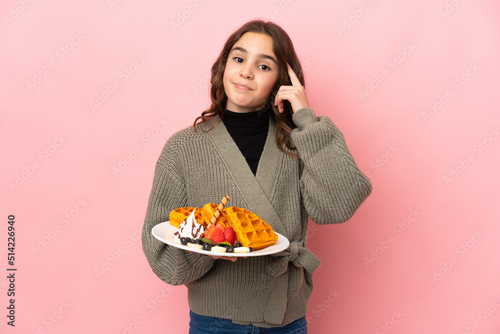 Little girl holding waffles isolated on pink background thinking an idea