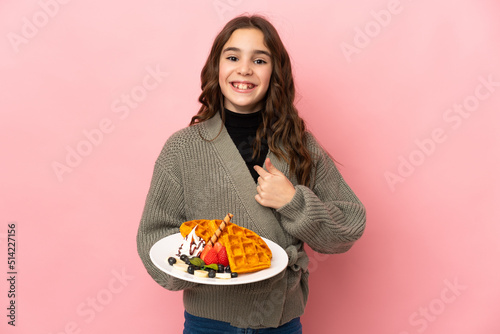 Little girl holding waffles isolated on pink background with surprise facial expression