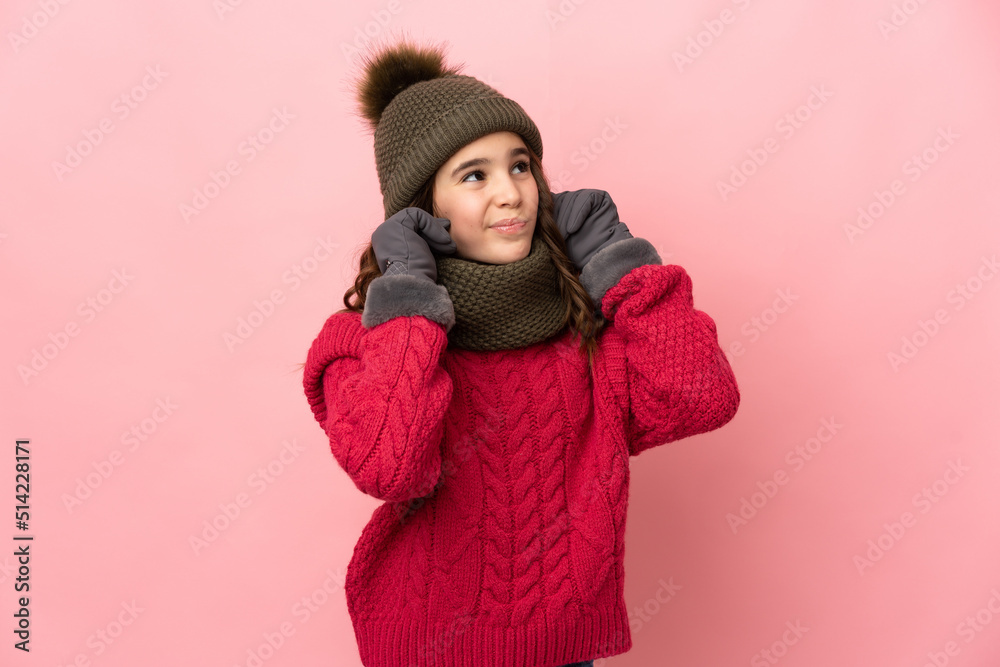 Little girl with winter hat isolated on pink background frustrated and covering ears Little girl with winter hat isolated on pink background frustrated and covering ears