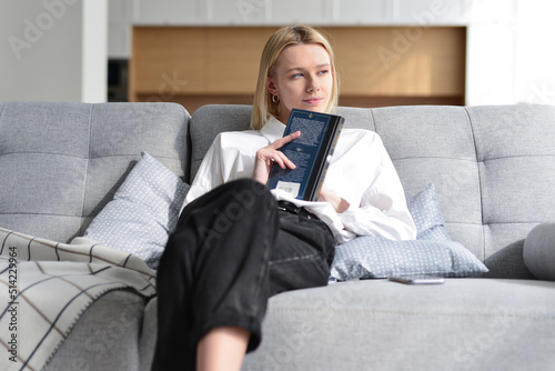 Tablou pe pânză Woman sits on couch brooding with book