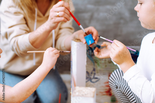 Woman educator conducting lesson with children in drawing in kindergarten. Little girls sitting and painting with paintbrush in playroom closeup. Children imagination, development of creative skills