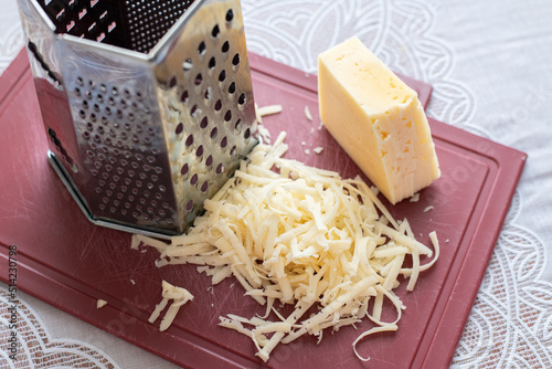 A pile of grated cheese on plastic board next to a grater photo