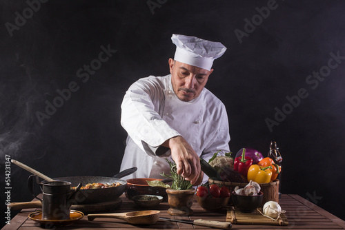 Male cook in white uniform and hat using aromatic herbs