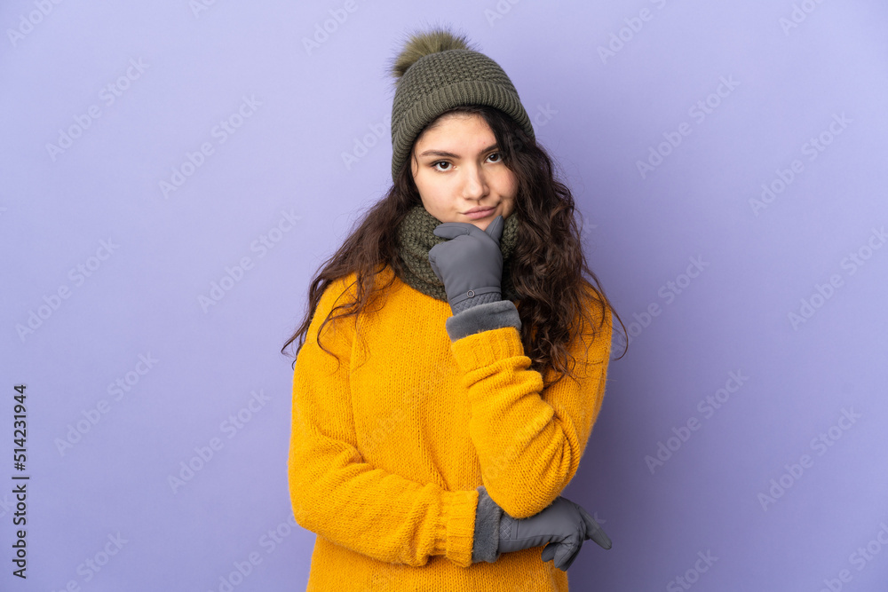 Teenager Russian girl with winter hat isolated on purple background thinking