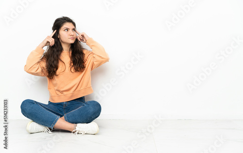 Teenager Russian girl sitting on the floor having doubts and thinking