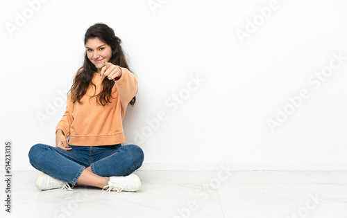 Teenager Russian girl sitting on the floor pointing front with happy expression
