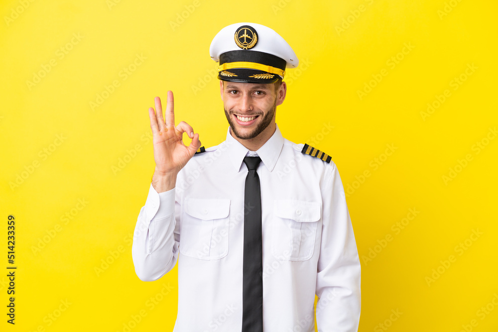 Airplane caucasian pilot isolated on yellow background showing ok sign with fingers