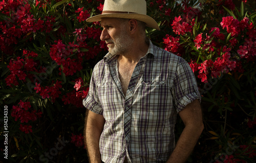 Portrait of adult man in sun hat and shirt against red flowers plants