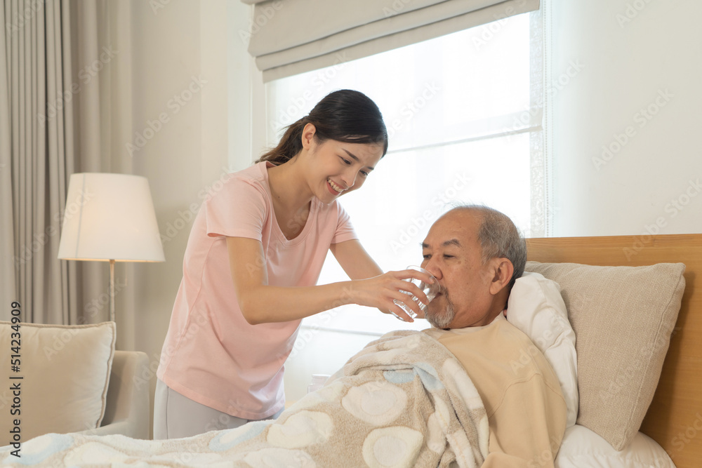 Fototapeta premium Happy woman nurse, daughter taking a medicine to sick old senior elderly patient lying on bed in bedroom in home or house in medical and healthcare treatment. Asian Thai people lifestyle. Family