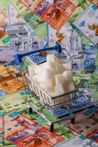 Pieces of refined sugar in a miniature supermarket shopping cart and Kazakh money