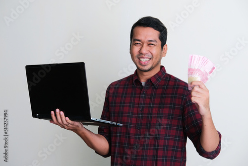Adult Asian man smiling while holding a laptop and money photo