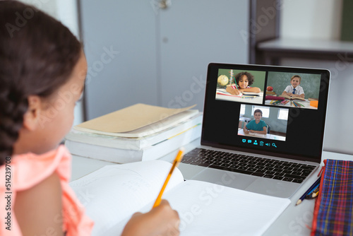 Asian girl writing in book while studying online through video call over laptop at home