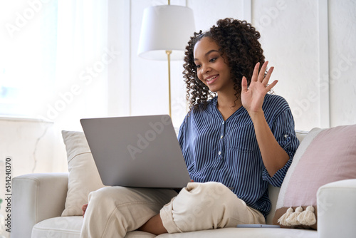Happy African American teen girl waving hand talking using laptop enjoying online virtual chat video call having distance conversation chat meeting sitting on sofa at home.