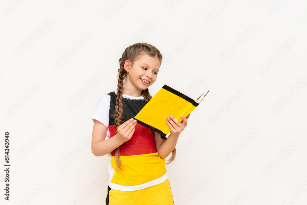 A little girl is reading a book on the German language. Courses on teaching German to children.A child in a jacket with a German flag. A little girl is reading a book on the German language. Courses on teaching German to children.A child in a jacket with a German flag.