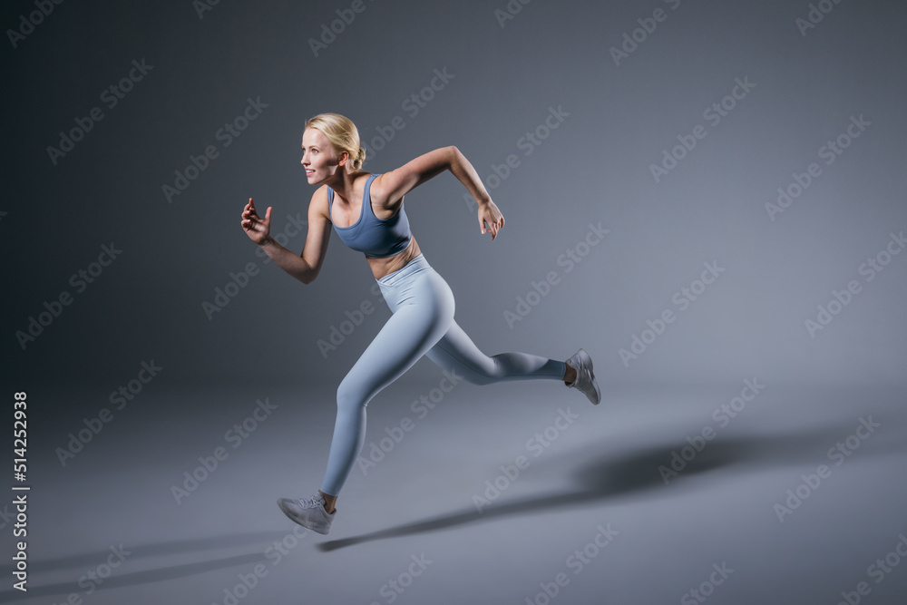 Women running in studio. Female runner on blue gray background. Healthy blonde woman. Profile view of sport runner. Full length of fit girl Women running in studio. Female runner on blue gray background. Healthy blonde woman. Profile view of sport runner. Full length of fit girl