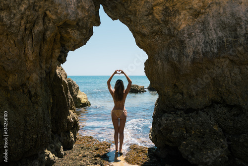 Woman in swimwear showing heart gesture at seaside