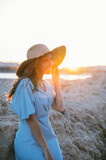 Content trendy woman smiling on rocky seashore at sunset