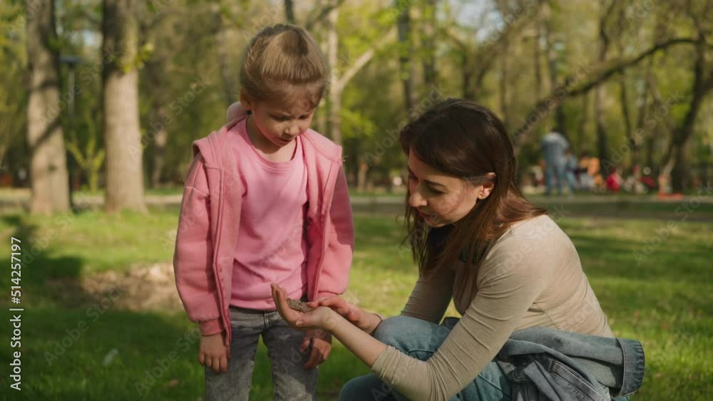 Mother shows large butterfly to curious little daughter in shady spring park. Woman and girl observe flying bug. Environmental education in town Mother shows large butterfly to curious little daughter in shady spring park. Woman and girl observe flying bug. Environmental education in town