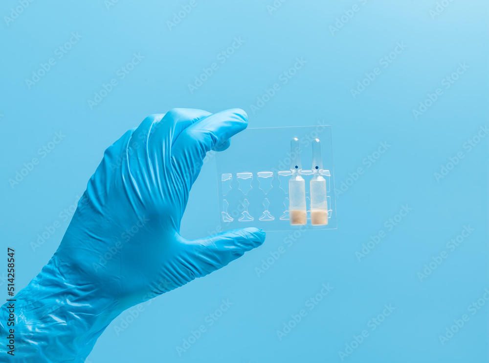 Medical glove. Ampoules with a white liquid in the hand in a blue medical glove. Isolated on a blue background. Medical glove. Ampoules with a white liquid in the hand in a blue medical glove. Isolated on a blue background.