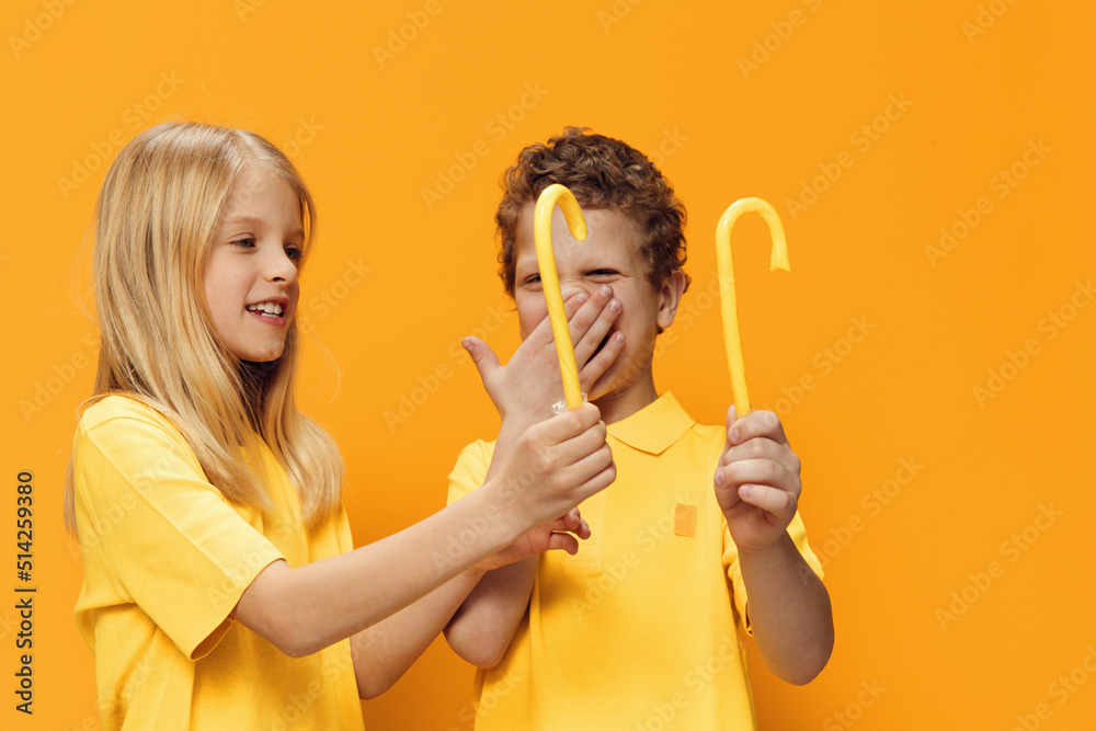joyful children stand with yellow candies and look at them cheerfully. Horizontal photo on a yellow background with empty space for an advertising layout joyful children stand with yellow candies and look at them cheerfully. Horizontal photo on a yellow background with empty space for an advertising layout