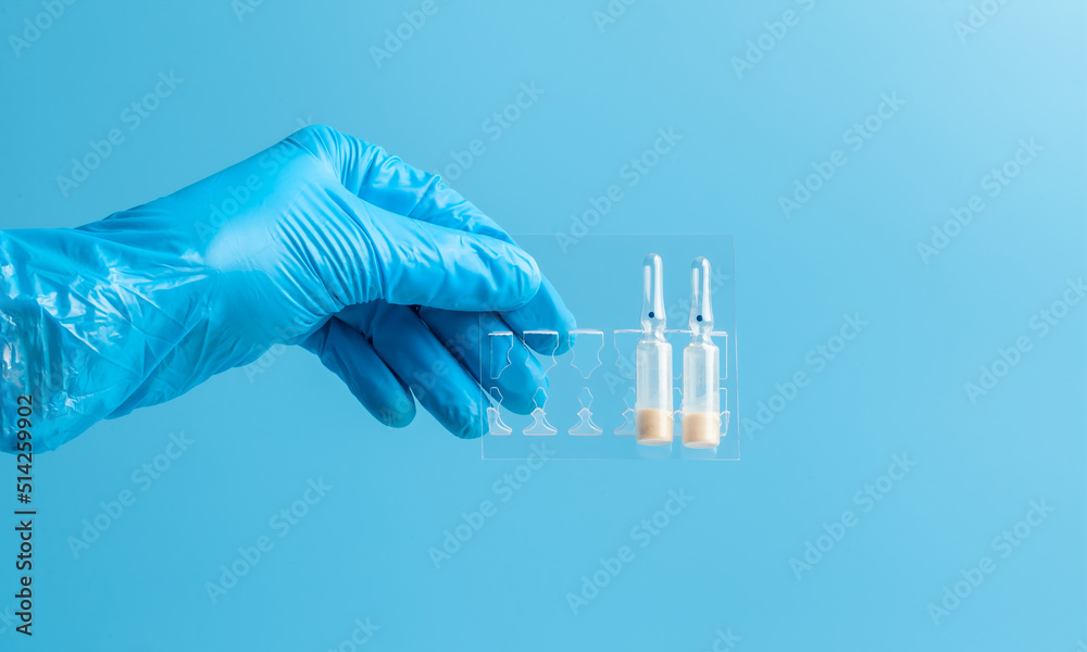 Medical glove. Ampoules with a white liquid in the hand in a blue medical glove. Isolated on a blue background.