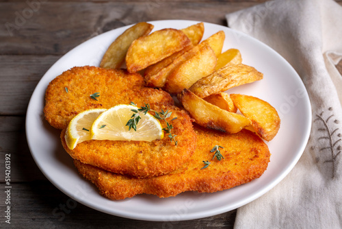 Vászonkép Chicken schnitzel with sauce, fried potatoes and lemon in a plate