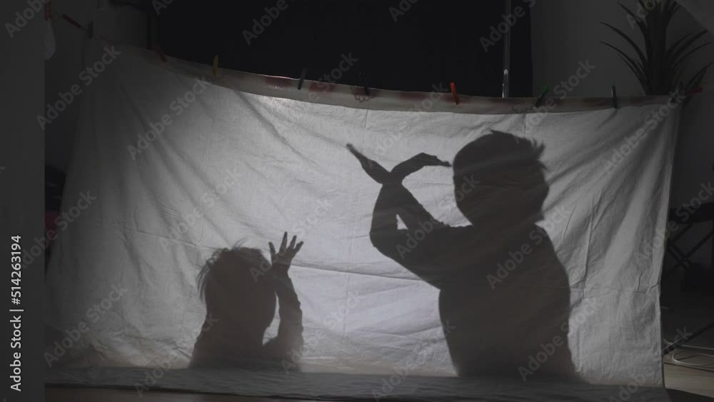 Brothers playing shadows on sheet tent lit by lamp in their room