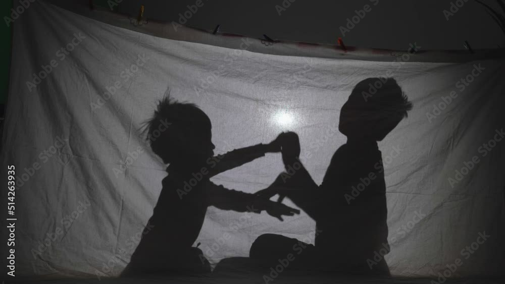 Children playing shadows on sheet tent lit by lamp in their room