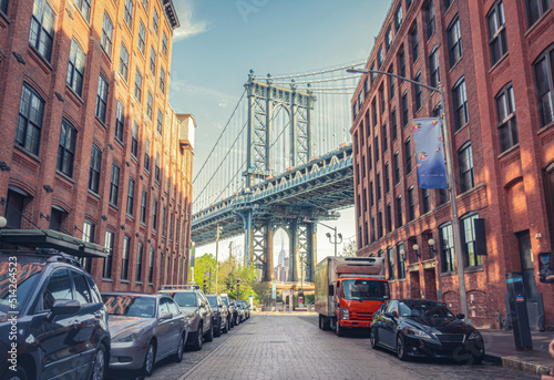 Manhattan Bridge between Manhattan and Brooklyn over East River seen from a narrow alley enclosed by two brick buildings on a sunny day in Washington street in Dumbo, Brooklyn, NYC © Argelis