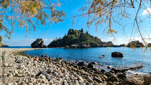 Panoramic view from the stone pebble beach Spiaggia di Isola Bella on the touristic paradise island Isola Bella in Taormina, Sicily, Italy, Europe, EU. Dreamy seascape at Ionian Mediterranean sea photo