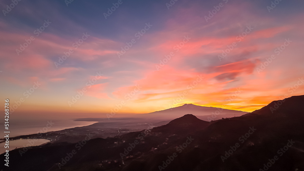 Panoramic view on silhouette of hills during twilight. Watching beautiful sunset behind volcano Mount Etna near Castelmola, Taormina, Sicily, Italy, Europe, EU. Clouds with vibrant red orange colors