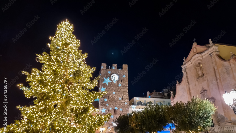 Naklejka premium Christmas tree, lights and decoration at night on the main square (Piazza IX Aprile) in Taormina, Province of Messina, Sicily, Italy, Europe, EU. Happy holidays at the Mediterranean sea