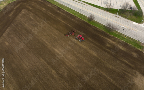 An aerial view above a field as a large, red tractor is seen sowing at the beginning of the farming season.